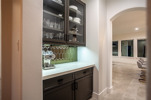 bar featuring dark brown cabinets, backsplash, and light tile patterned floors