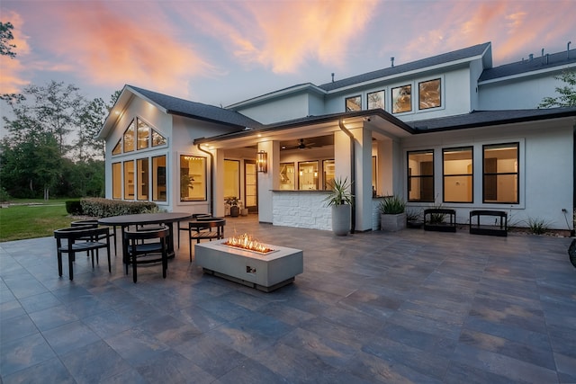 back house at dusk featuring a fire pit, ceiling fan, and a patio