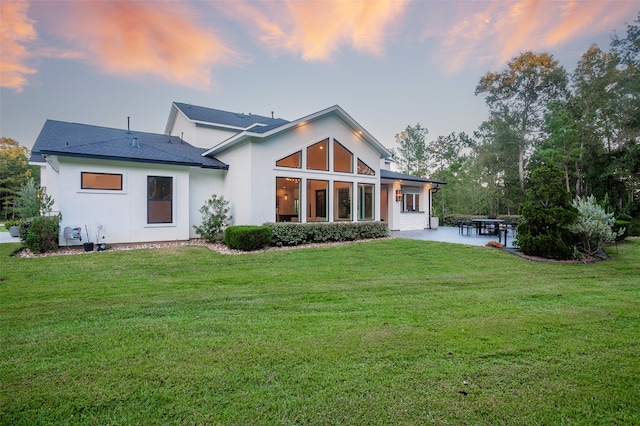 back house at dusk featuring a patio area and a yard