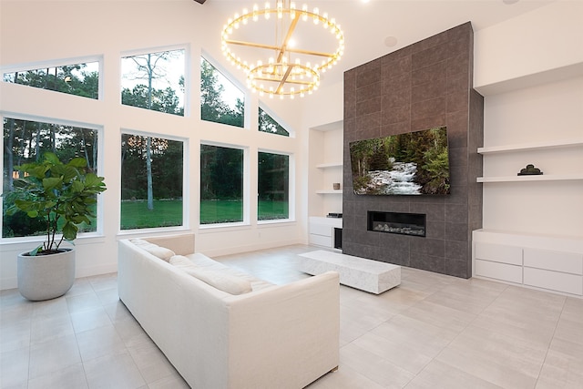 living room featuring built in shelves, a tile fireplace, an inviting chandelier, a high ceiling, and light tile patterned flooring