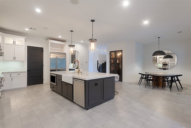 kitchen featuring a center island with sink, white cabinetry, sink, and hanging light fixtures