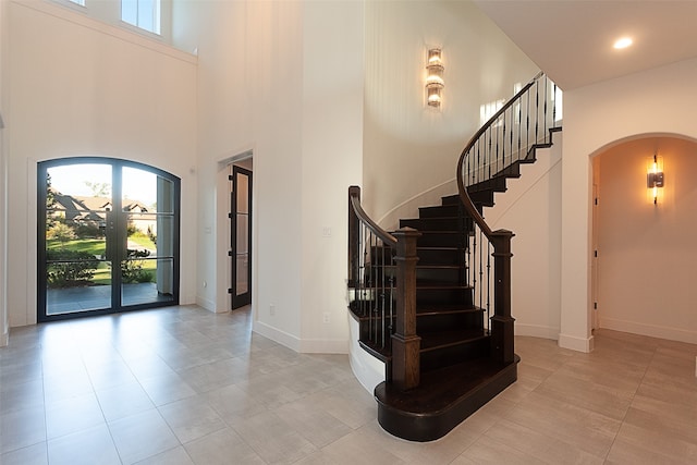 entrance foyer with light tile patterned flooring, a towering ceiling, and french doors