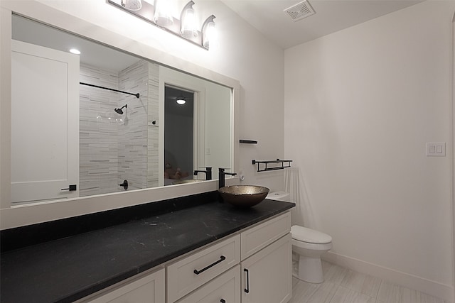 bathroom featuring a tile shower, vanity, and toilet