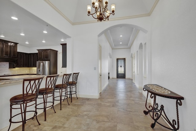 kitchen featuring stainless steel fridge, backsplash, dark brown cabinetry, pendant lighting, and a notable chandelier