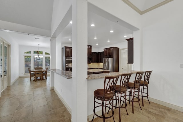 kitchen featuring an inviting chandelier, stainless steel fridge, dark brown cabinetry, light stone countertops, and kitchen peninsula