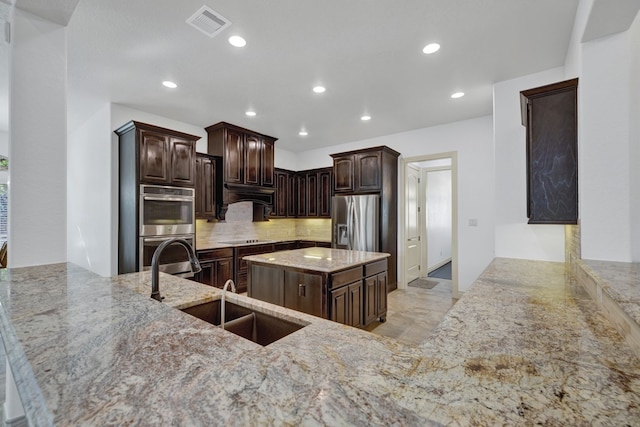 kitchen with dark brown cabinetry, sink, stainless steel appliances, light stone counters, and backsplash