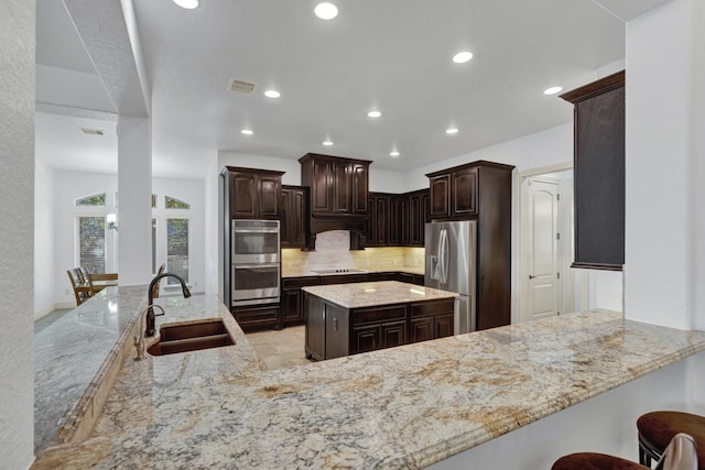 kitchen featuring sink, dark brown cabinetry, light stone counters, kitchen peninsula, and stainless steel appliances