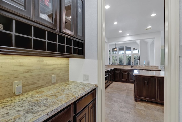 kitchen with backsplash, light stone counters, dark brown cabinetry, and sink