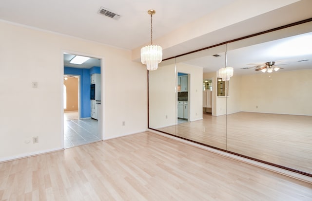 empty room featuring ceiling fan with notable chandelier and light hardwood / wood-style flooring