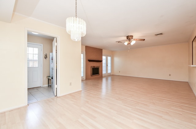 unfurnished living room with a fireplace, ceiling fan with notable chandelier, and light wood-type flooring