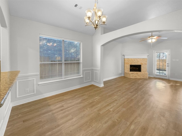 unfurnished living room featuring ceiling fan with notable chandelier, a stone fireplace, lofted ceiling, and light hardwood / wood-style flooring