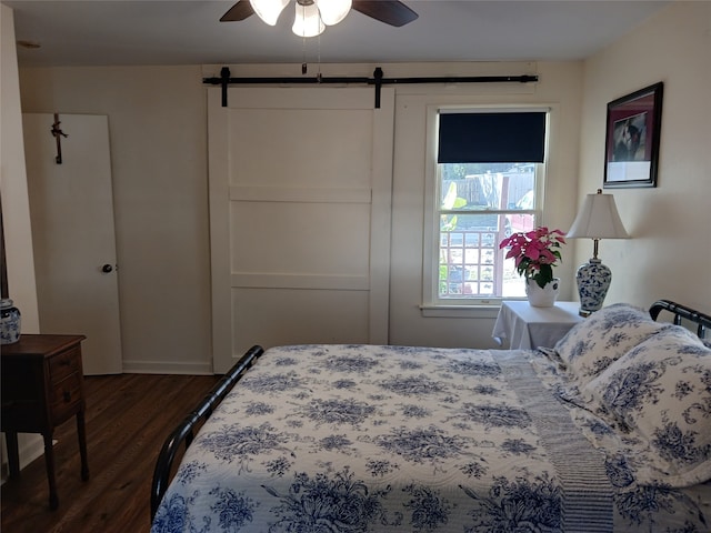 bedroom with a barn door, ceiling fan, and dark wood-type flooring