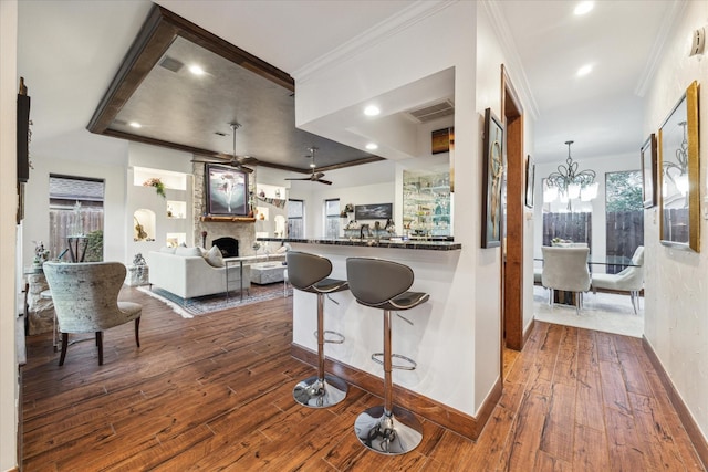 kitchen featuring a large fireplace, hanging light fixtures, crown molding, dark hardwood / wood-style floors, and ceiling fan with notable chandelier