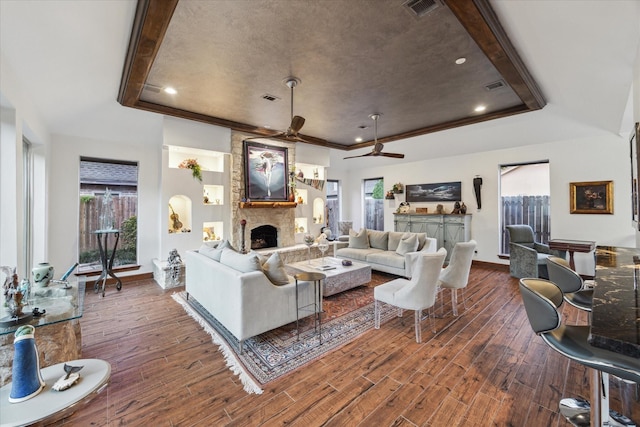 living room with ceiling fan, a stone fireplace, and a raised ceiling