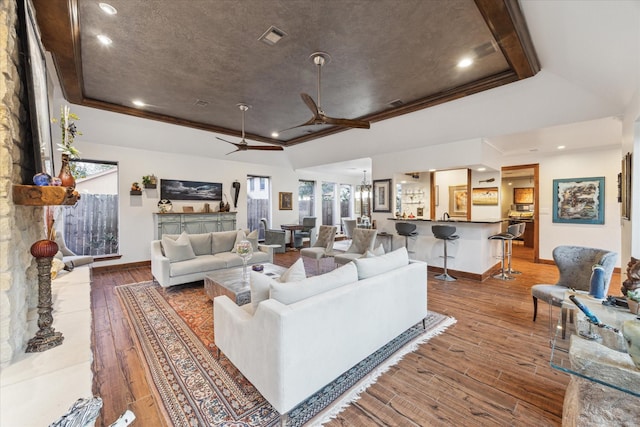 living room featuring hardwood / wood-style flooring, a raised ceiling, ceiling fan, and a stone fireplace