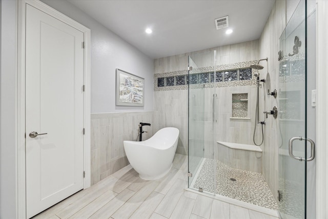 bathroom featuring shower with separate bathtub and tile walls