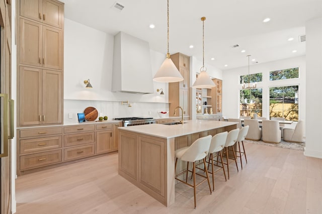 kitchen featuring pendant lighting, custom exhaust hood, sink, a large island, and light hardwood / wood-style floors