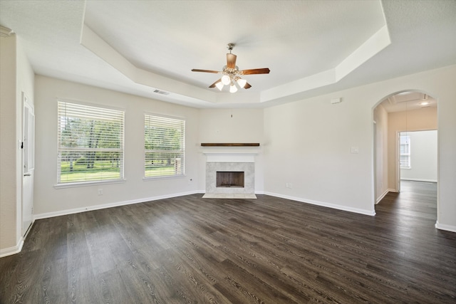 unfurnished living room with a raised ceiling, a tile fireplace, ceiling fan, and dark wood-type flooring