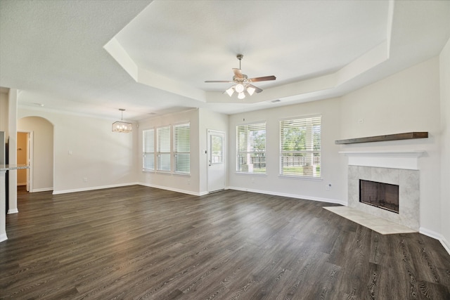 unfurnished living room with a raised ceiling, ceiling fan, dark hardwood / wood-style flooring, and a tile fireplace