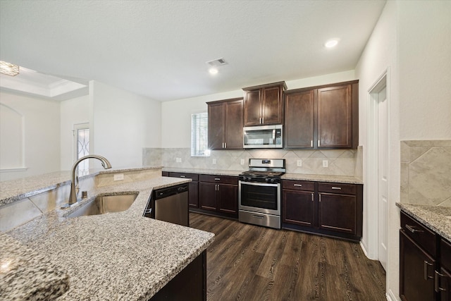 kitchen with appliances with stainless steel finishes, dark hardwood / wood-style floors, sink, dark brown cabinetry, and light stone countertops