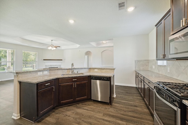 kitchen featuring sink, light stone counters, dark brown cabinets, appliances with stainless steel finishes, and a raised ceiling