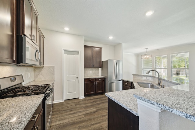 kitchen with hanging light fixtures, sink, light stone counters, appliances with stainless steel finishes, and dark hardwood / wood-style flooring