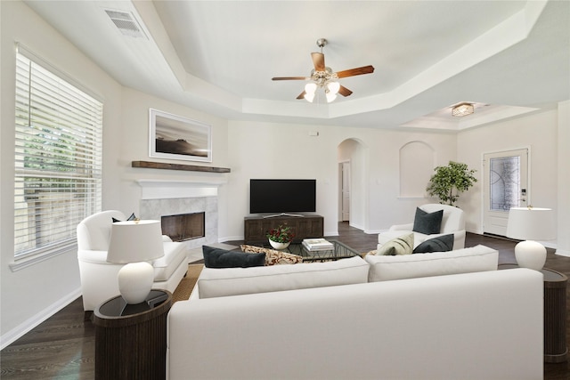 living room featuring dark wood-type flooring, ceiling fan, a fireplace, and a raised ceiling