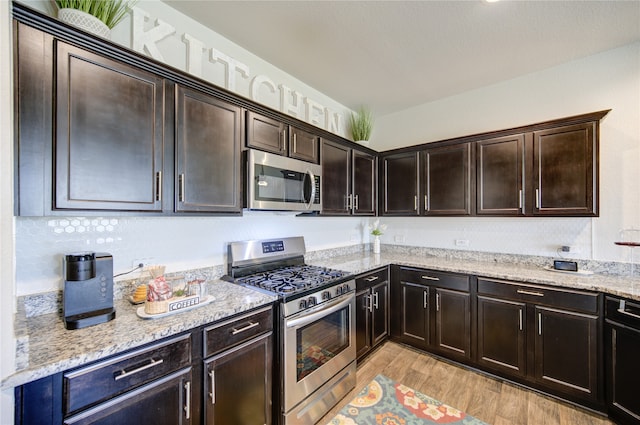 kitchen featuring light stone counters, dark brown cabinetry, appliances with stainless steel finishes, and light hardwood / wood-style flooring