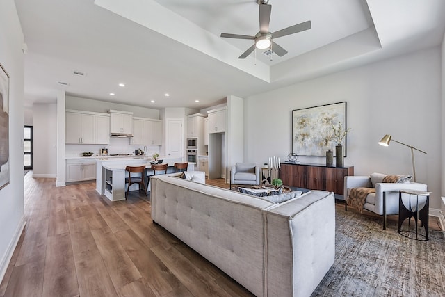 living room featuring a tray ceiling, ceiling fan, and hardwood / wood-style flooring