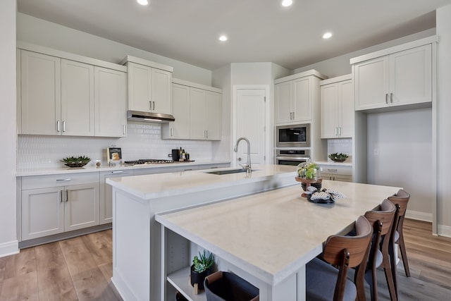 kitchen featuring sink, a center island with sink, appliances with stainless steel finishes, and light wood-type flooring