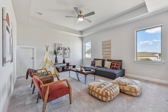 living room featuring a tray ceiling, light carpet, and ceiling fan