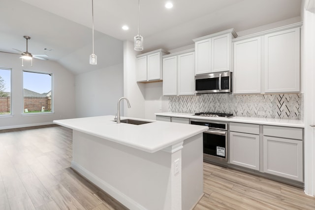 kitchen with hanging light fixtures, stainless steel appliances, light hardwood / wood-style floors, vaulted ceiling, and a center island with sink