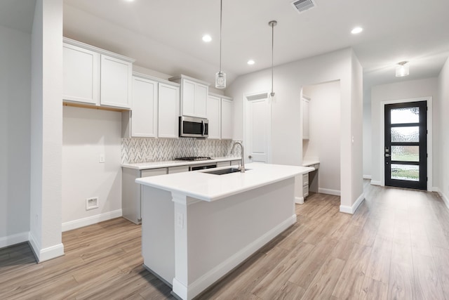 kitchen with a kitchen island with sink, white cabinets, stainless steel appliances, and decorative light fixtures