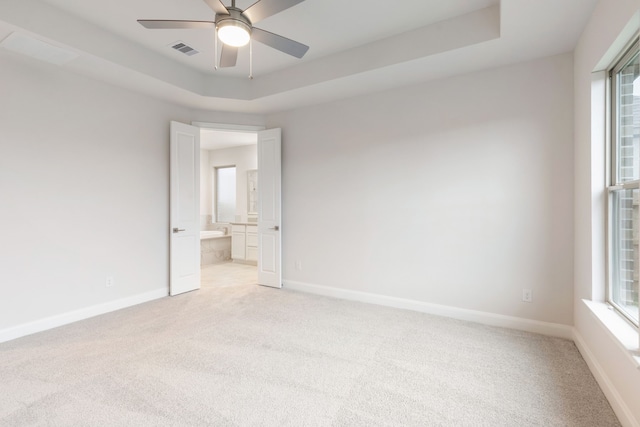 carpeted spare room featuring a tray ceiling, ceiling fan, and a healthy amount of sunlight