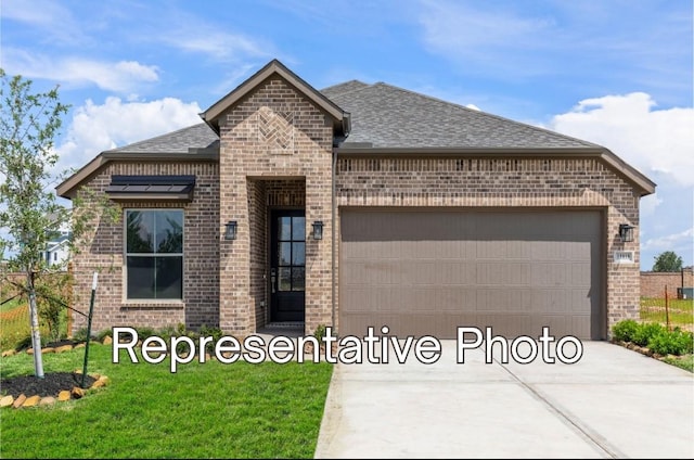 french country home featuring roof with shingles, concrete driveway, a front lawn, a garage, and brick siding