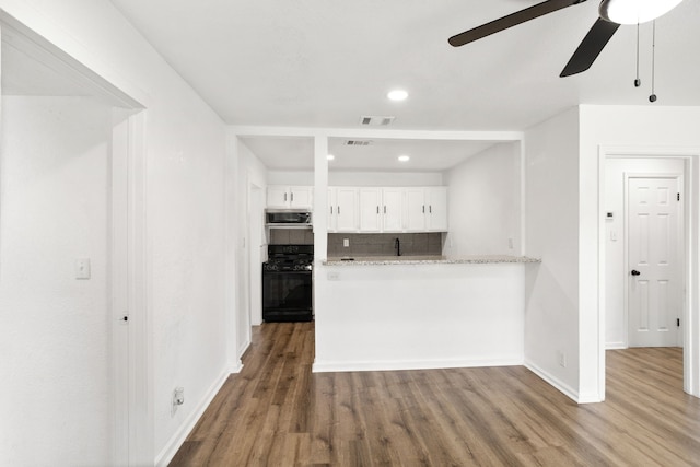 kitchen with white cabinetry, black gas range oven, light stone counters, decorative backsplash, and hardwood / wood-style flooring