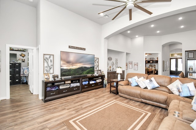 living room featuring a high ceiling, ceiling fan with notable chandelier, french doors, and wood-type flooring