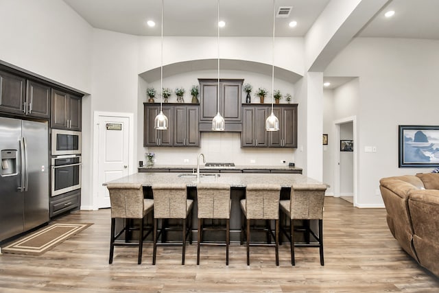 kitchen featuring a kitchen breakfast bar, a kitchen island with sink, light hardwood / wood-style floors, and appliances with stainless steel finishes