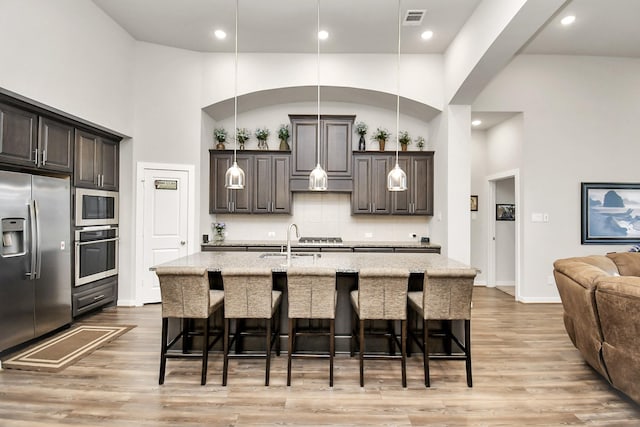 kitchen featuring an island with sink, appliances with stainless steel finishes, a breakfast bar, and dark brown cabinets