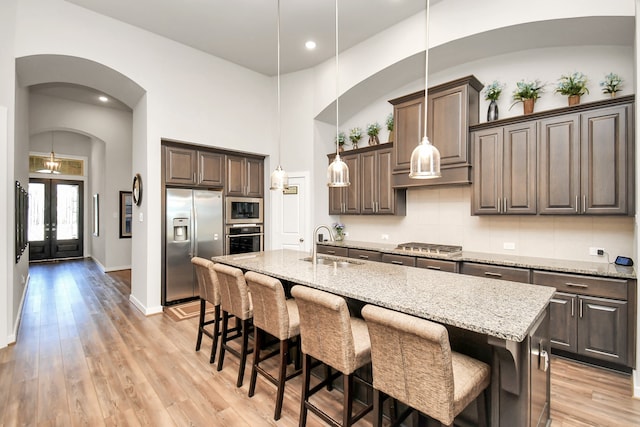 kitchen with pendant lighting, a center island with sink, sink, light hardwood / wood-style flooring, and appliances with stainless steel finishes