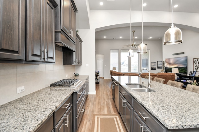 kitchen with light stone countertops, light wood-type flooring, sink, decorative light fixtures, and an island with sink