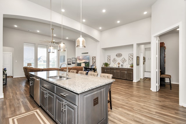 kitchen featuring a breakfast bar, a center island with sink, stainless steel dishwasher, ceiling fan, and dark hardwood / wood-style flooring