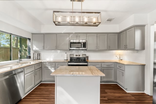 kitchen with gray cabinetry, stainless steel appliances, light stone counters, dark hardwood / wood-style flooring, and a kitchen island