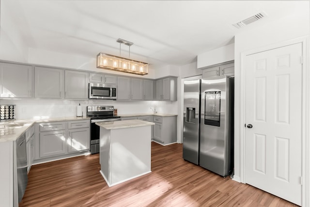 kitchen with stainless steel appliances, decorative light fixtures, gray cabinets, a kitchen island, and hardwood / wood-style flooring