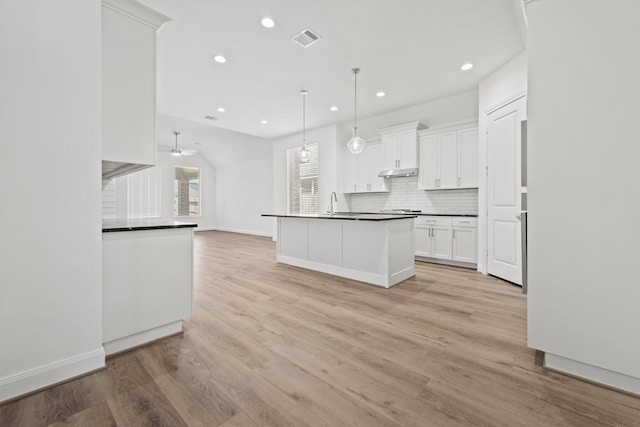 kitchen featuring visible vents, under cabinet range hood, dark countertops, light wood-style floors, and decorative backsplash