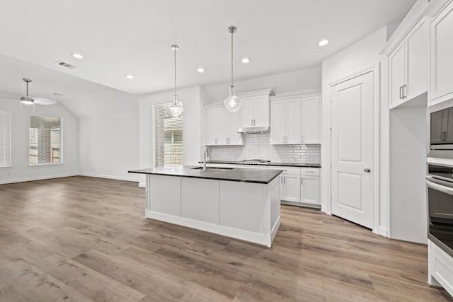 kitchen with dark countertops, visible vents, under cabinet range hood, decorative backsplash, and appliances with stainless steel finishes