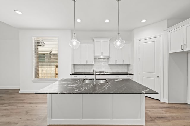 kitchen with a sink, under cabinet range hood, backsplash, white cabinetry, and light wood finished floors