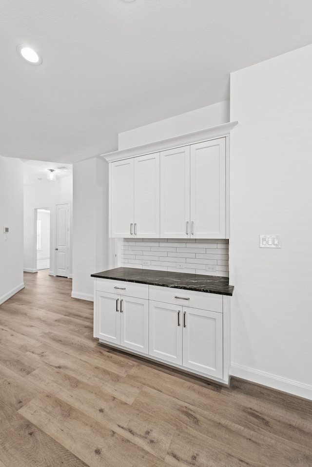 kitchen with baseboards, decorative backsplash, light wood-style floors, white cabinetry, and dark countertops