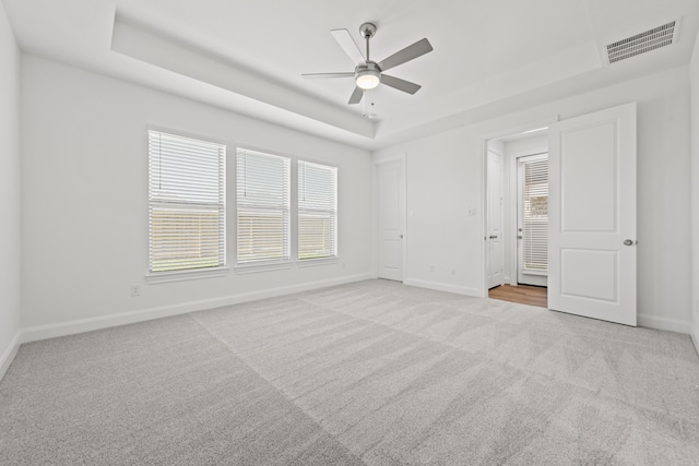 unfurnished bedroom featuring visible vents, a raised ceiling, a ceiling fan, carpet floors, and baseboards