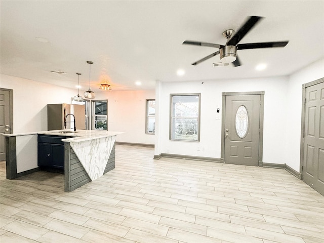 kitchen featuring pendant lighting, stainless steel fridge, a kitchen island with sink, ceiling fan, and sink